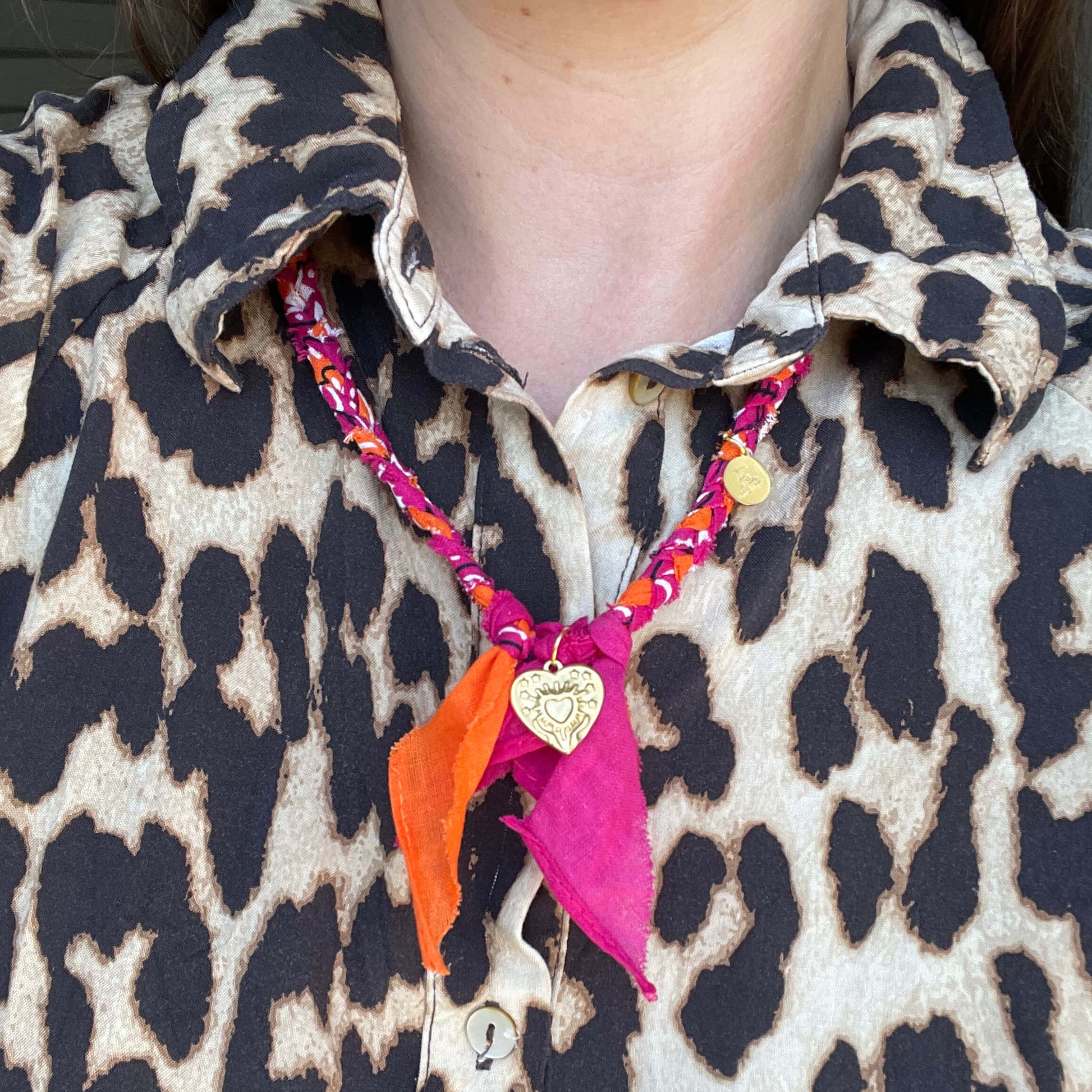 Handgemaakte bandana ketting in fuchsia en oranje met gouden bedels, gedragen bij een panterprint blouse.