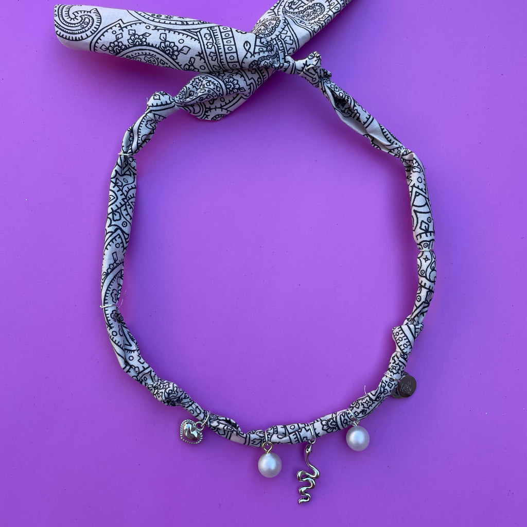 Geknoopte wit-zwarte bandana ketting met zilveren bedels en parels, ideaal voor een bohemian festivalstijl of casual zomerse outfits.