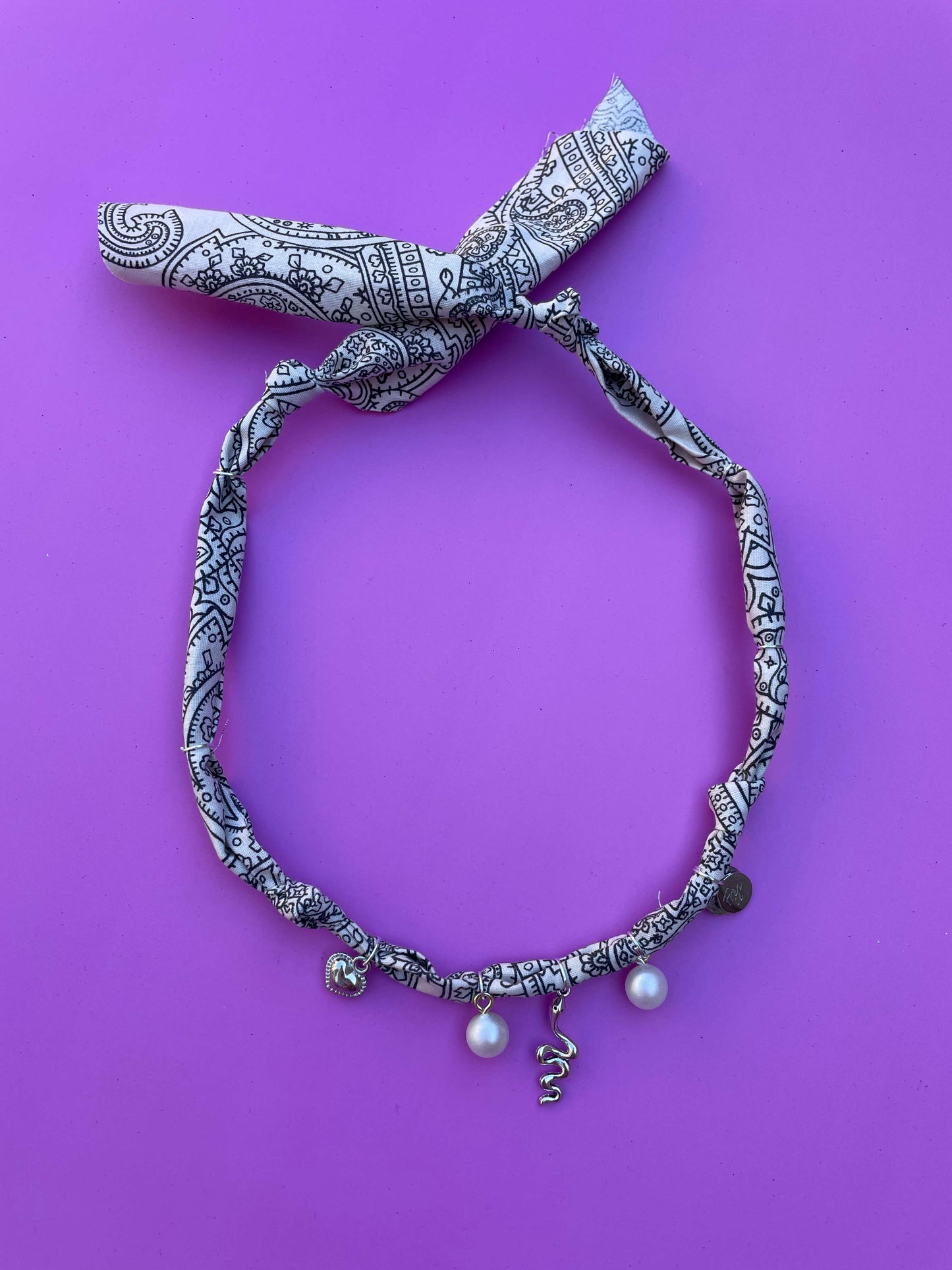 Geknoopte wit-zwarte bandana ketting met zilveren bedels en parels, ideaal voor een bohemian festivalstijl of casual zomerse outfits.