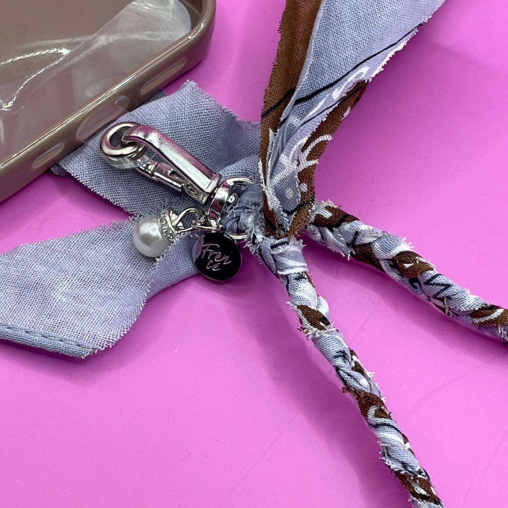 Close-up van blauw en bruin bandana telefoonkoord, met zilveren charms en stevig ontwerp, ideaal voor het dragen van je telefoon handsfree.