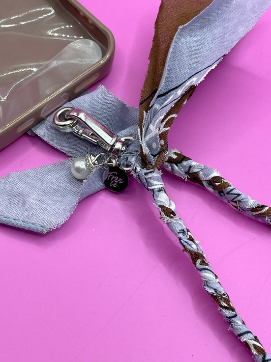 Close-up van blauw en bruin bandana telefoonkoord, met zilveren charms en stevig ontwerp, ideaal voor het dragen van je telefoon handsfree.