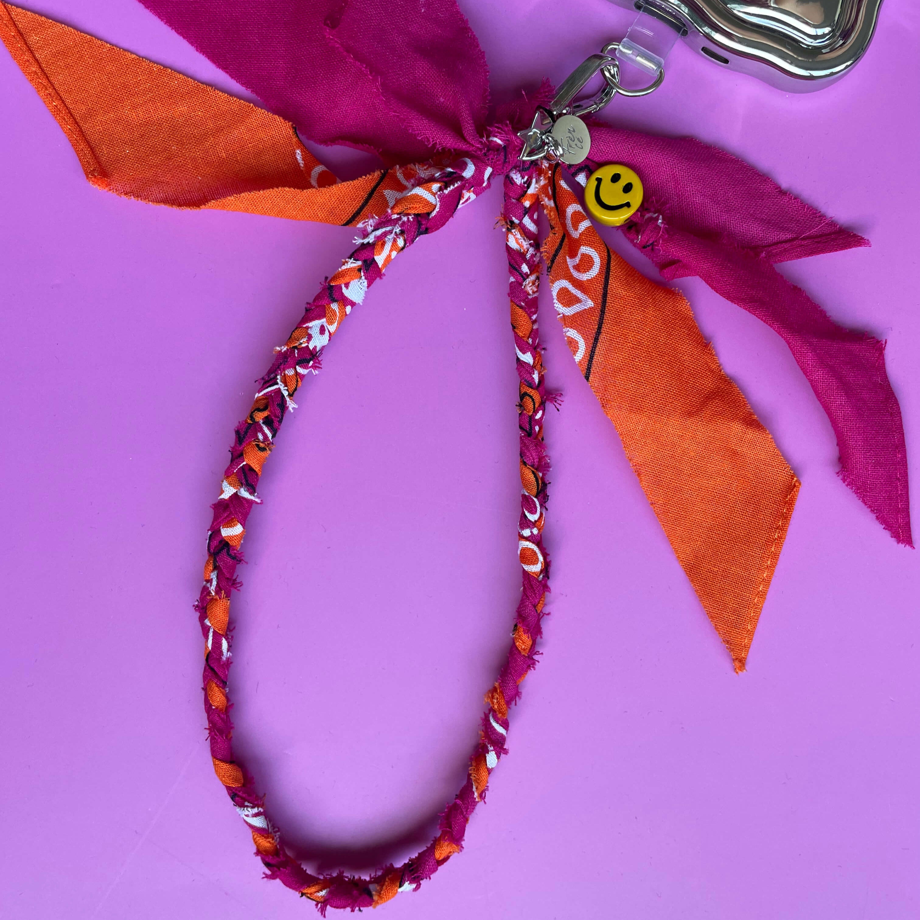 Fuchsia en oranje telefoonkoordje met smiley bevestigd aan een telefoonhoesje