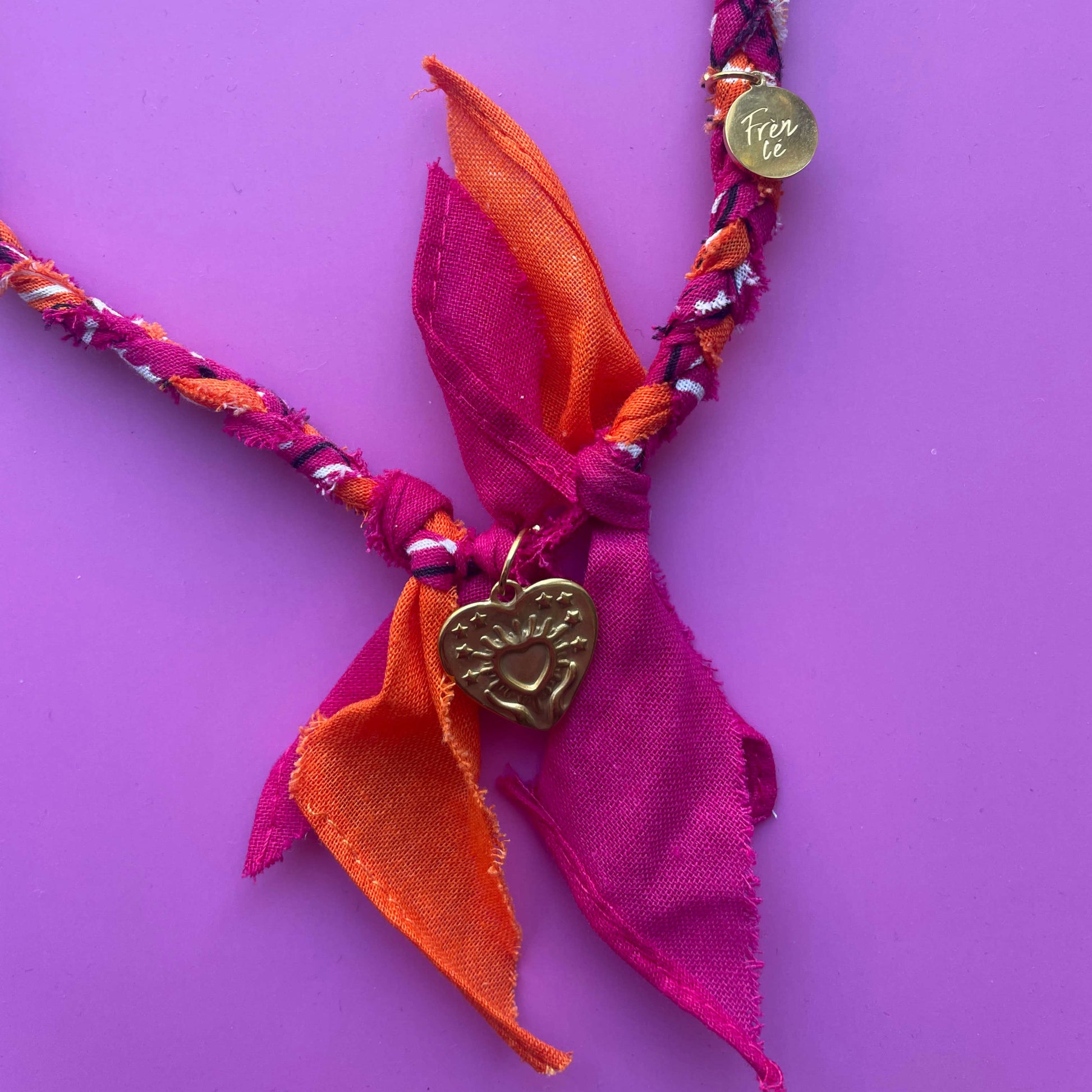 Close-up van de fuchsia-oranje bandana ketting met gouden hartvormige bedel van 100% katoen – uniek handgemaakt accessoire.