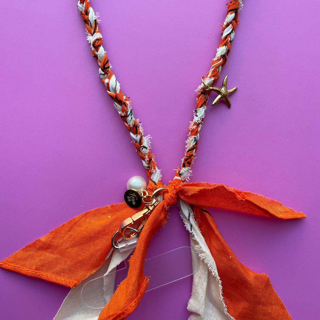 Close-up van gouden bedels, zeester en parel aan het oranje en beige bandana telefoonkoord kort voor aan iedere telefoon